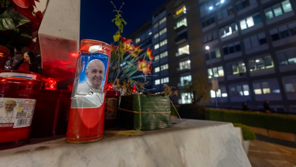 Votive candles, including some bearing a photo of Pope Francis, are seen on the base of a statue of St. John Paul II outside Rome's Gemelli hospital Feb. 15, 2025. (CNS photo/Pablo Esparza)